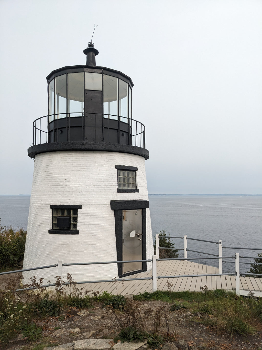 Lighthouse with a white exterior and black accents, situated on a coastal area.