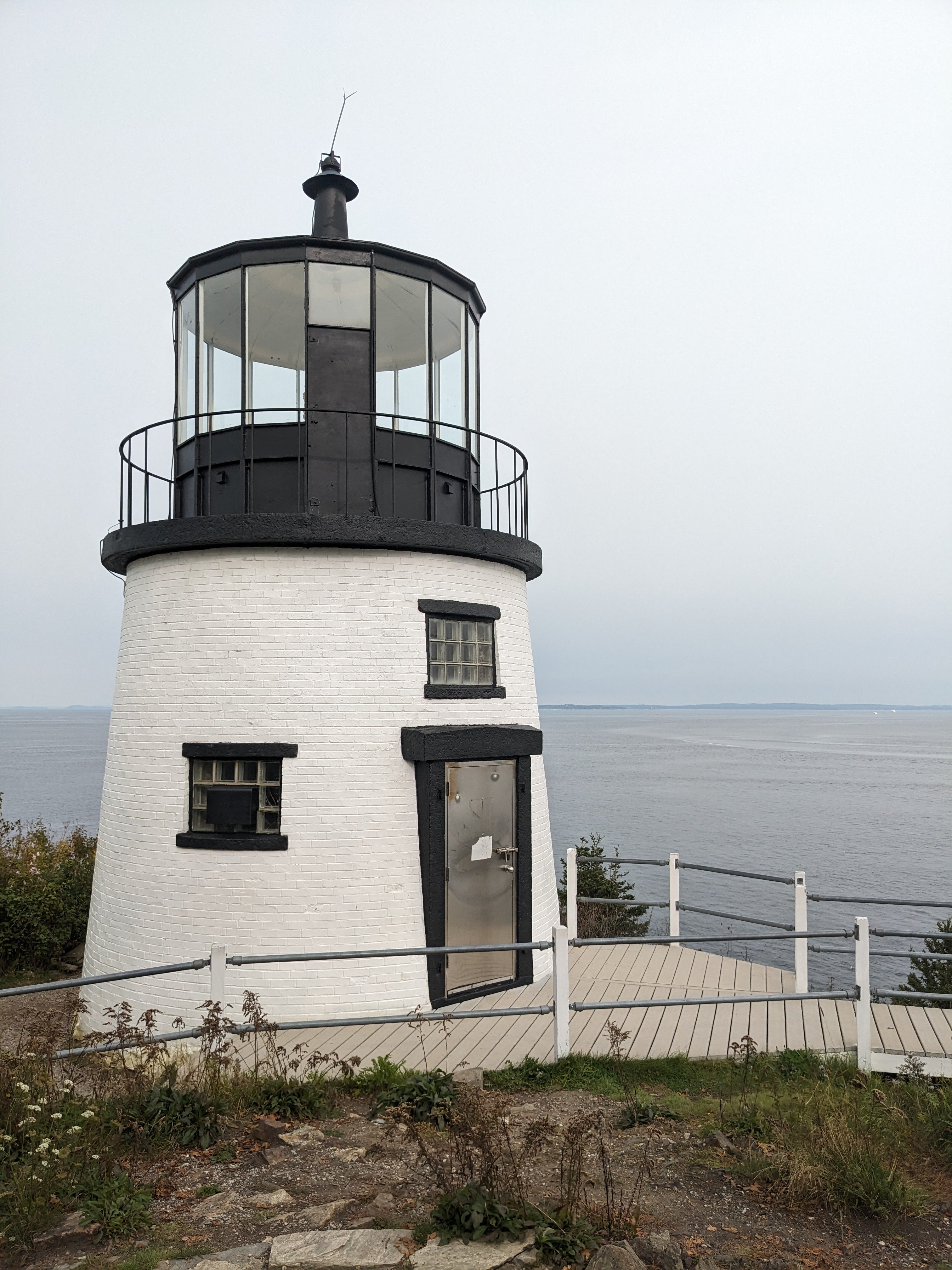 Lighthouse with a white exterior and black accents, situated on a coastal area.
