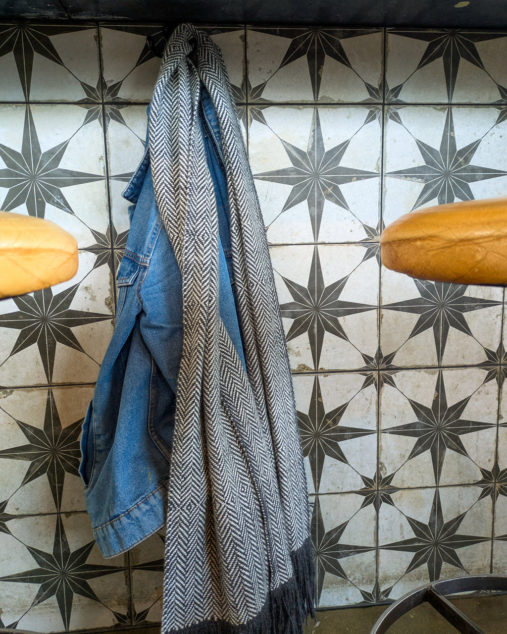 Blue denim jacket and patterned scarf hanging on a tiled wall with star designs.