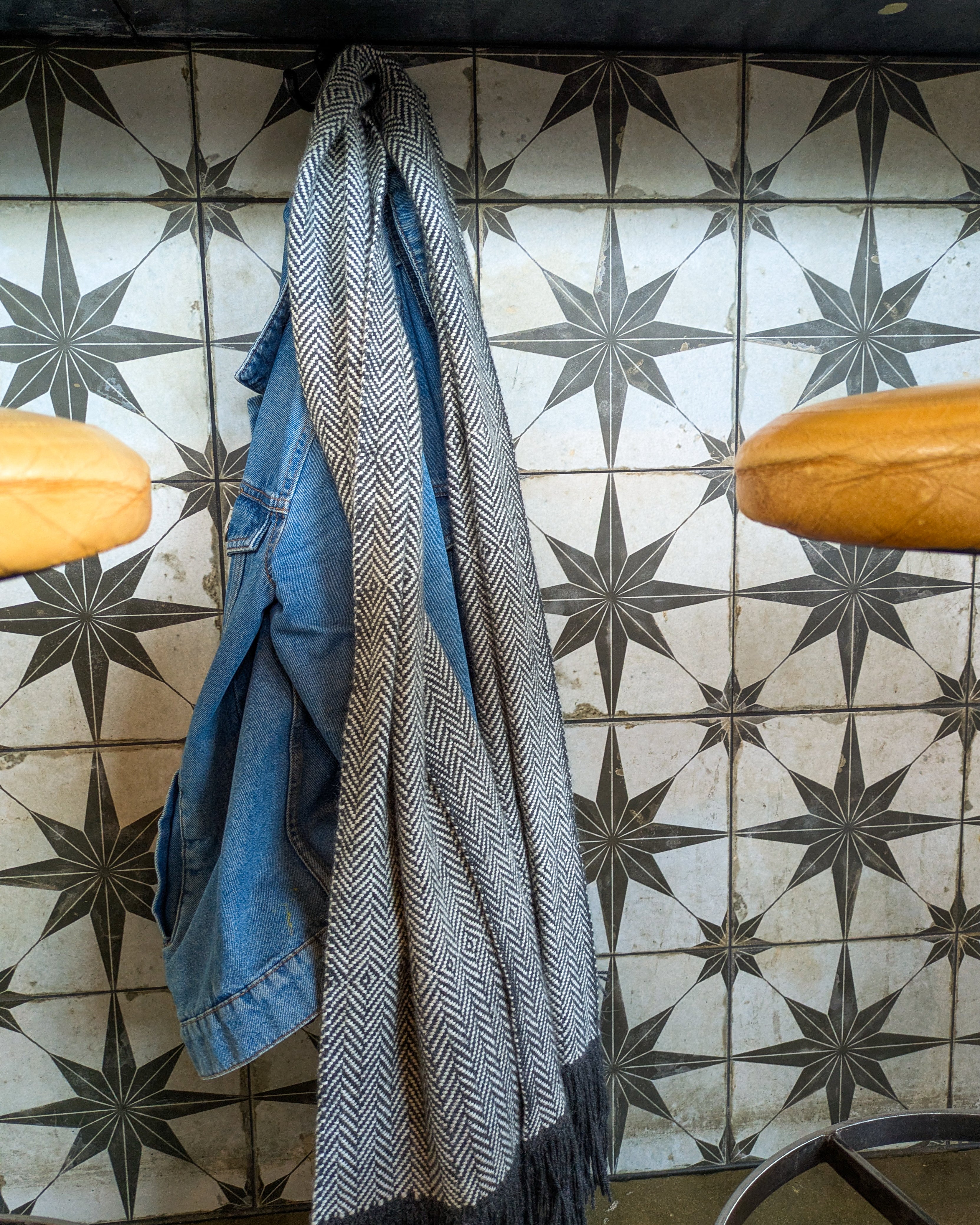 Blue denim jacket and patterned scarf hanging on a tiled wall with star designs.