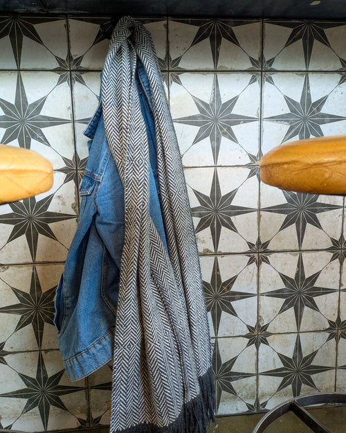 Blue denim jacket and patterned scarf hanging on a tiled wall with star designs.