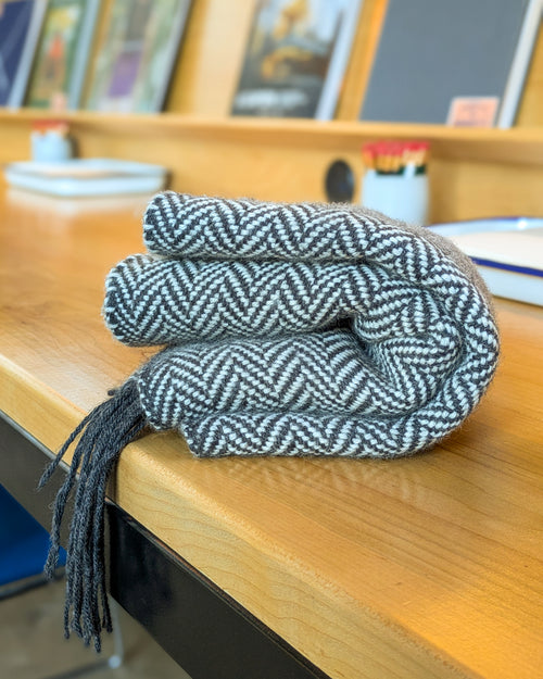 Coiled black and white herringbone-patterned scarf on a wooden surface with blurred background